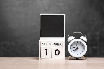 Calendar with september 10 date and alarm clock on table against chalk board background