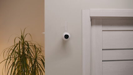 Installed security camera on the wall in the modern apartment. CCTV camera with microphone and motion sensor. Concept of monitoring system, surveillance, safety and personal privacy.