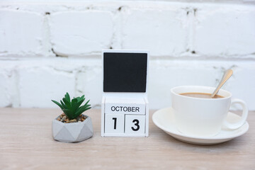 Wooden calendar with date October 13 and plant with coffee cup on table against brick wall background. Deadline, planning, business concept