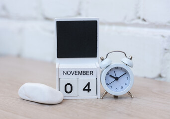 Wooden calendar with date November 04 and alarm clock on table against brick wall background. Deadline, planning, business concept