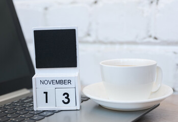 Wooden calendar with date November 13 and laptop, coffee cup on table against brick wall background. Deadline, planning, business concept