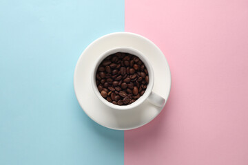 Ceramic coffee cup with coffee beans on pink blue background. Top view