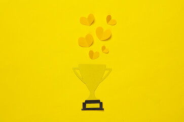 Paper-cut golden winner trophy cup with hearts on yellow background. Competition, sport, prize,...