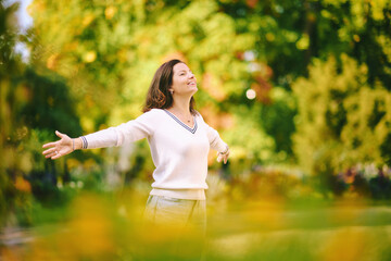 Outdoor portrait of happy and healthy 40 - 45 year old woman enjoying nice sunny day in park, arms wide open - 575053955