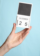 Female hand holding wooden calendar with date december 25 isolated on blue background