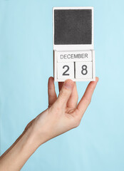 Female hand holding wooden calendar with date december 28 isolated on blue background