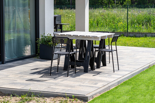 Terrace table made of white pallet standing on plastic trestles, black plastic chairs. - Powered by Adobe