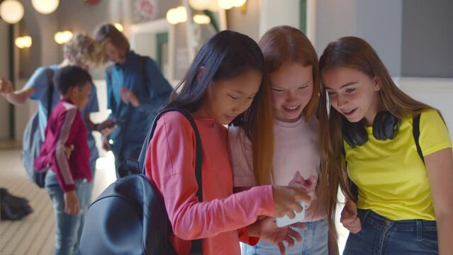 Happy young girls teenagers share an interesting app on smartphone and smile at school. Realtime