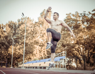 Athletic man with a naked torso practicing jumping up, warming up before running to the stadium. Healthy lifestyle