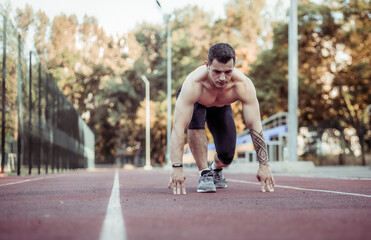 Athletic man preparing to run low start sprint at stadium