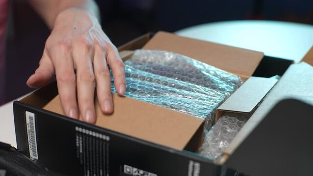 Extreme close up of unrecognizable man open cardboard box with new power supply new at home sitting at desk. Stages of upgrading or assembling desktop computer. Shooting in slow motion.