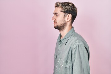 Hispanic man with beard standing over pink background looking to side, relax profile pose with natural face with confident smile.
