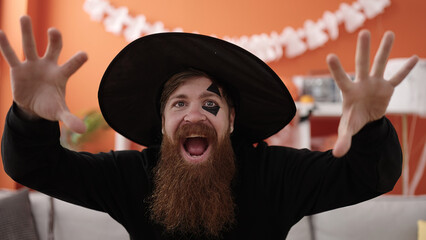 Young redhead man wearing wizard costume doing scare expression at home