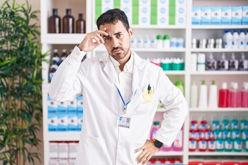 Handsome hispanic man working at pharmacy drugstore worried and stressed about a problem with hand on forehead, nervous and anxious for crisis