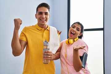 Young couple wearing sportswear and headphones celebrating victory with happy smile and winner expression with raised hands