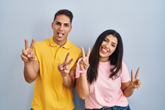 Young couple standing over isolated background smiling with tongue out showing fingers of both hands doing victory sign. number two.