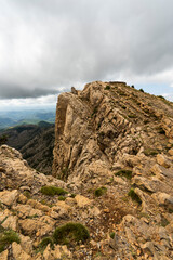 imagen de la cima de una monta&ntilde;a rocosa, con poca vegetaci&oacute;n y el cielo nublado