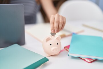 Young hispanic girl inserting coin on piggy bank at home