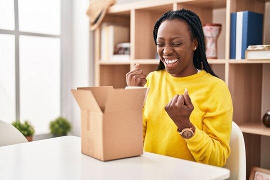 Beautiful Black Woman Opening Cardboard Box Celebrating Surprised And Amazed For Success With Arms Raised And Eyes Closed