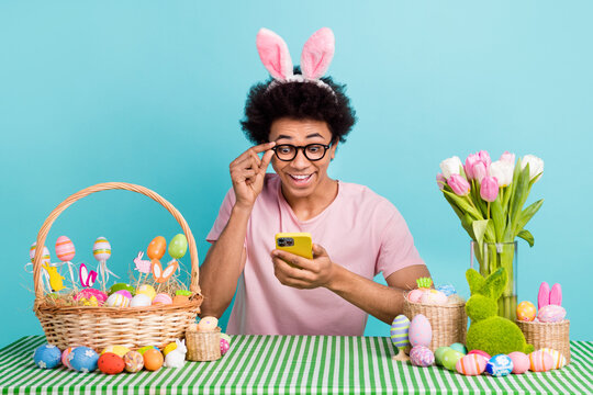 Photo of young surprised student wear rabbit ears touch glasses smartphone good news bucket eggs tulips bouquet isolated on cyan color background - Powered by Adobe