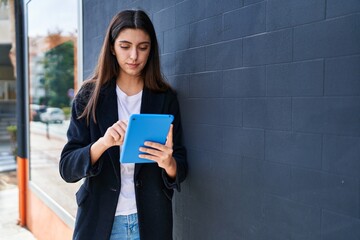 Young beautiful hispanic woman using touchpad with serious expression at street