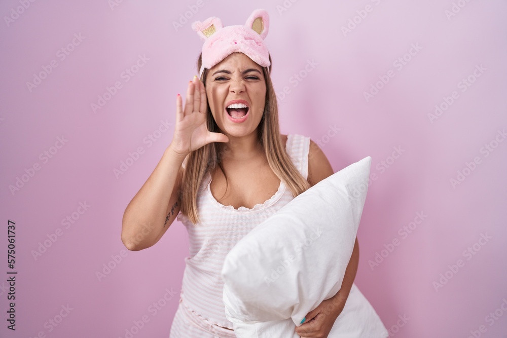 Sticker Young blonde woman wearing pyjama hugging pillow shouting and screaming loud to side with hand on mouth. communication concept.