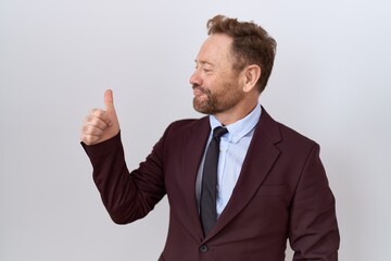 Middle age business man with beard wearing suit and tie looking proud, smiling doing thumbs up gesture to the side