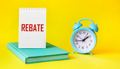 The word REBATE on a notebook and a yellow background, next to a clock and a diary