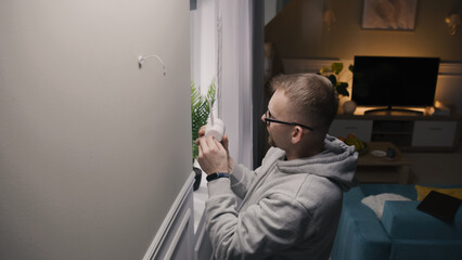 Man puts security camera on wall mount in living room and connects it to cable. He sets up CCTV camera for night using digital tablet and app. Concept of tracking system, safety and personal privacy.