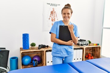 Young beautiful hispanic woman physiotherapist smiling confident holding document at rehab clinic