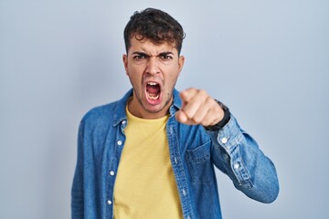 Young hispanic man standing over blue background pointing displeased and frustrated to the camera, angry and furious with you