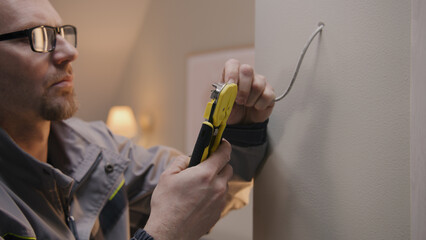 Close up shot of repairman in uniform and glasses works with cable twisted pair. Electrician removes insulation from wire with professional tool in the apartment. Installation of the Internet.