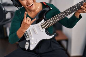 Obraz premium Young beautiful hispanic woman musician playing electrical guitar doing rock symbol with fingers at music studio