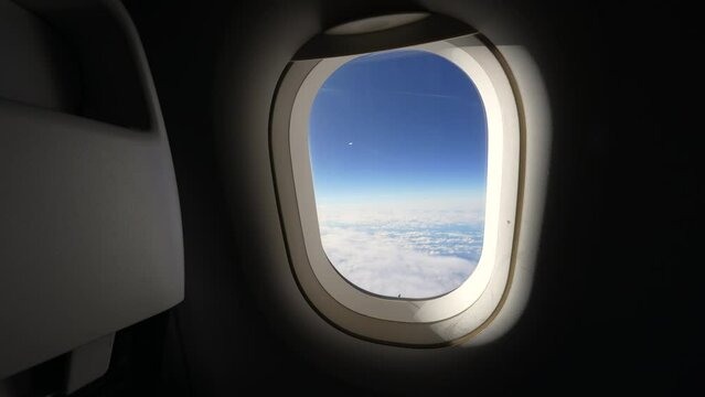Airplane window in the air high above. Passenger plane POV looking out at beautiful blue sky view