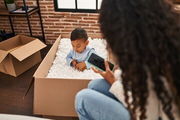 Mother and son using smartphone playing with ball sitting on sofa at new home