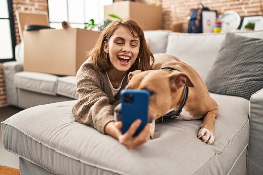Young caucasian woman make selfie by the smartphone lying on sofa with dog at new home