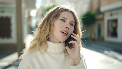 Young blonde woman talking on the smartphone with relaxed expression at street