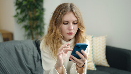 Young blonde woman using smartphone and credit card sitting on sofa at home