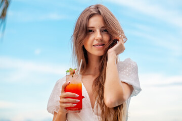 Young woman in a white dress lounges on the beach with a cocktail - Powered by Adobe