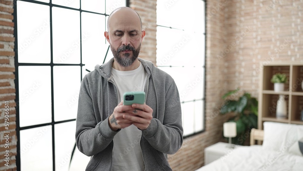 Sticker Young bald man using smartphone standing at bedroom