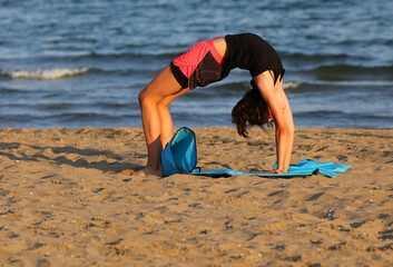 girl training by the sea in summer on the gym mat on the beach at sunset