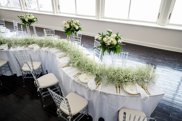 Event table setting with wine glasses, acrylic flower stands, baby's breath and candles on S curve table.