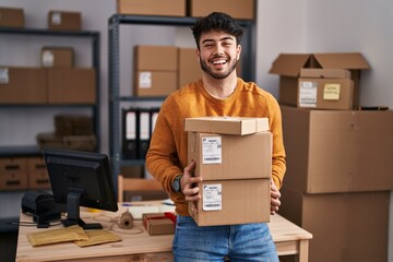 Hispanic man with beard working at small business ecommerce holding packages celebrating crazy and amazed for success with open eyes screaming excited. - obrazy, fototapety, plakaty