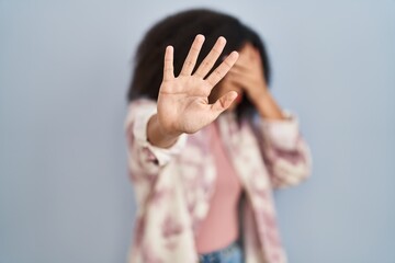 Young african american woman standing over blue background covering eyes with hands and doing stop gesture with sad and fear expression. embarrassed and negative concept.