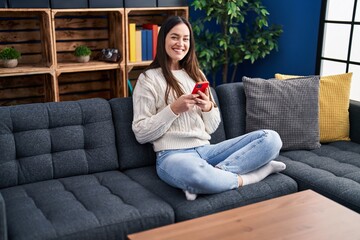 Obraz premium Young woman using smartphone sitting on sofa at home