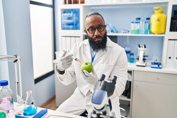 African american man working at scientist laboratory with apple relaxed with serious expression on face. simple and natural looking at the camera.