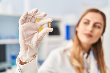 Young blonde woman wearing scientist uniform holding pill at laboratory