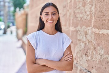 Young beautiful hispanic woman standing with arms crossed gesture at street