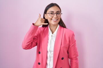 Young hispanic woman wearing business clothes and glasses smiling doing phone gesture with hand and fingers like talking on the telephone. communicating concepts.