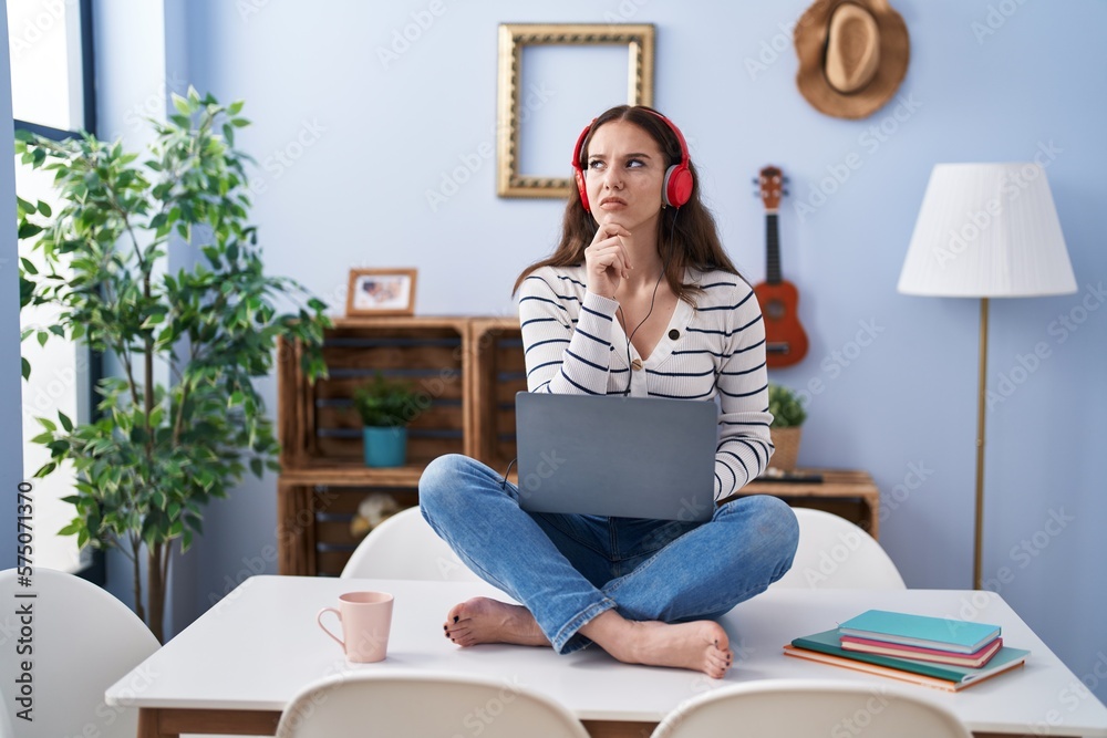 Sticker Young hispanic girl using laptop at home serious face thinking about question with hand on chin, thoughtful about confusing idea